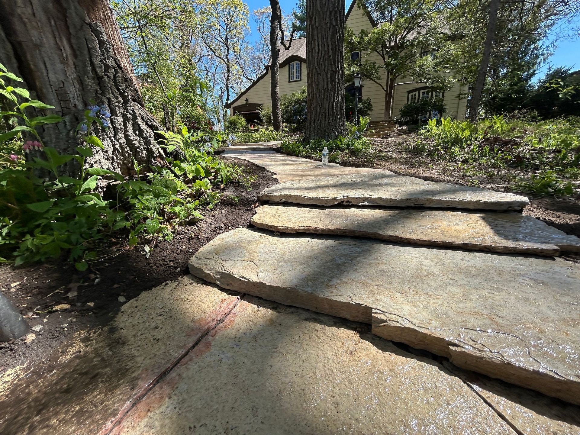 Patio paved with gray bricks, adjacent to a dark gray house with lit windows and a sliding glass door.