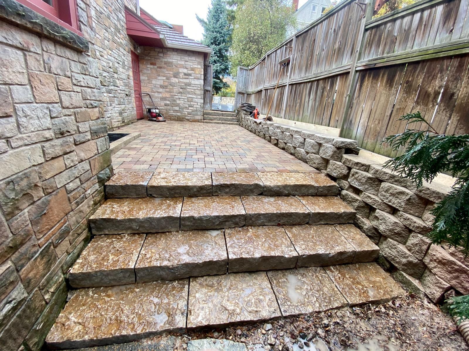 Stone steps and walkway leading up to a building, flanked by a stone wall and wooden fence.