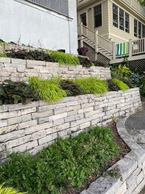 Stone retaining wall with tiered landscaping, featuring green and yellow plants.