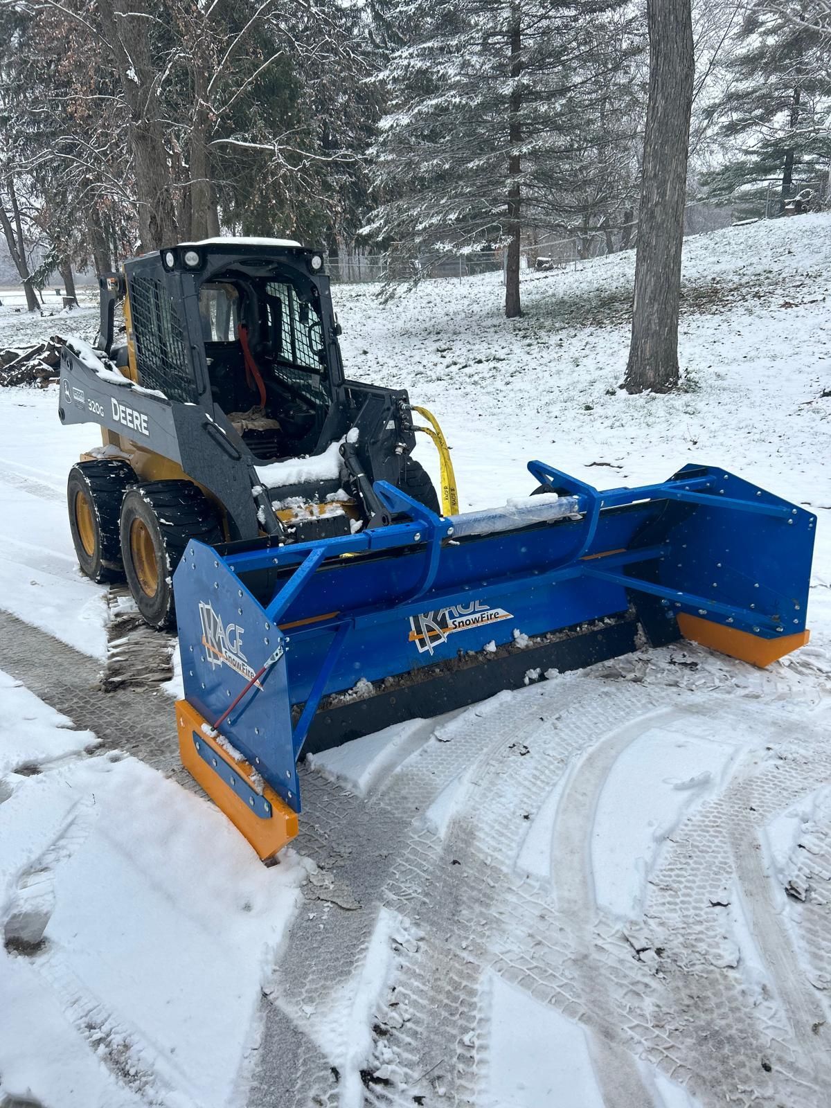 Yellow and black John Deere skid steer with blue snow blade clearing snow on a driveway.