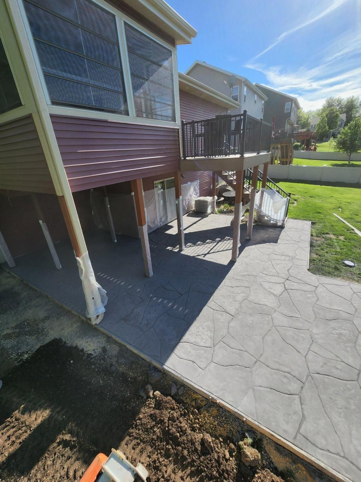 A backyard with a two-story deck over a concrete patio, sunny day.