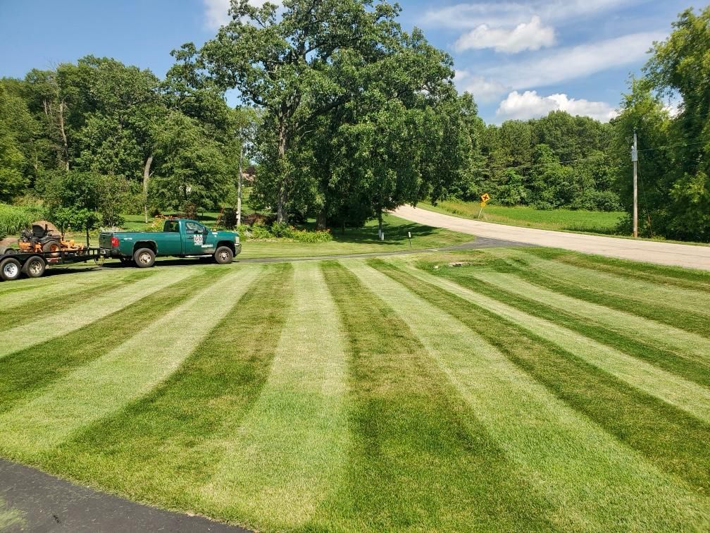 Green lawn with striped mowing pattern, a green truck, and a trailer.