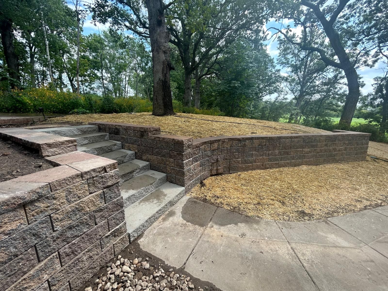 Stone steps and a retaining wall with gravel surrounding a tree in an outdoor setting.