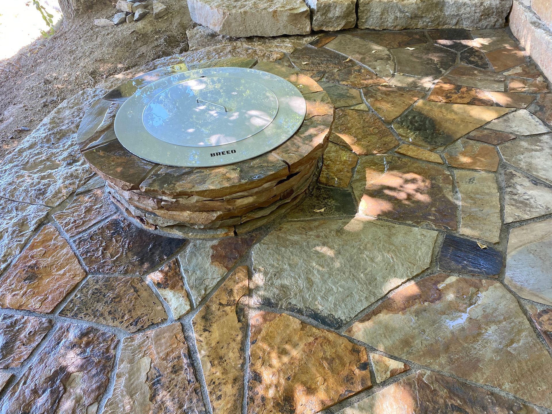 Fire pit with stone surround and flagstone patio. A gray metal lid sits atop the pit.