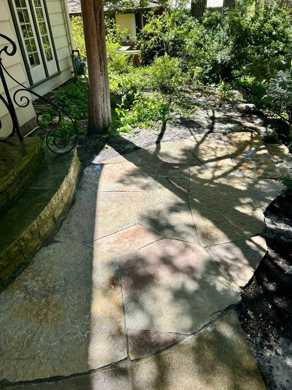 A stone path leads from a house doorway towards a shaded garden, with a tree in the center.