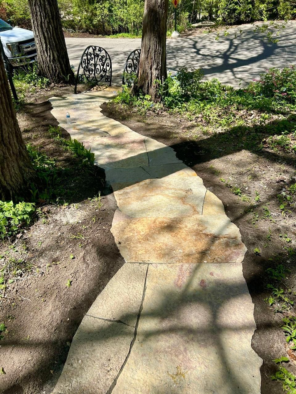 Stone walkway through the yard, bordered by trees and greenery, leading to a bench.