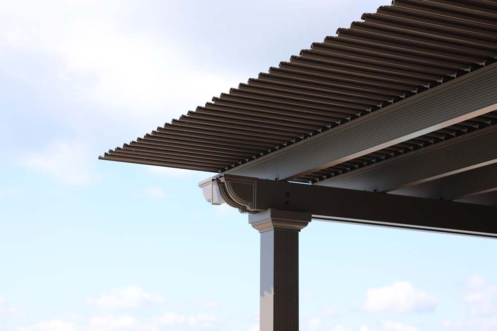 Brown pergola roof with gutter against a cloudy blue sky.
