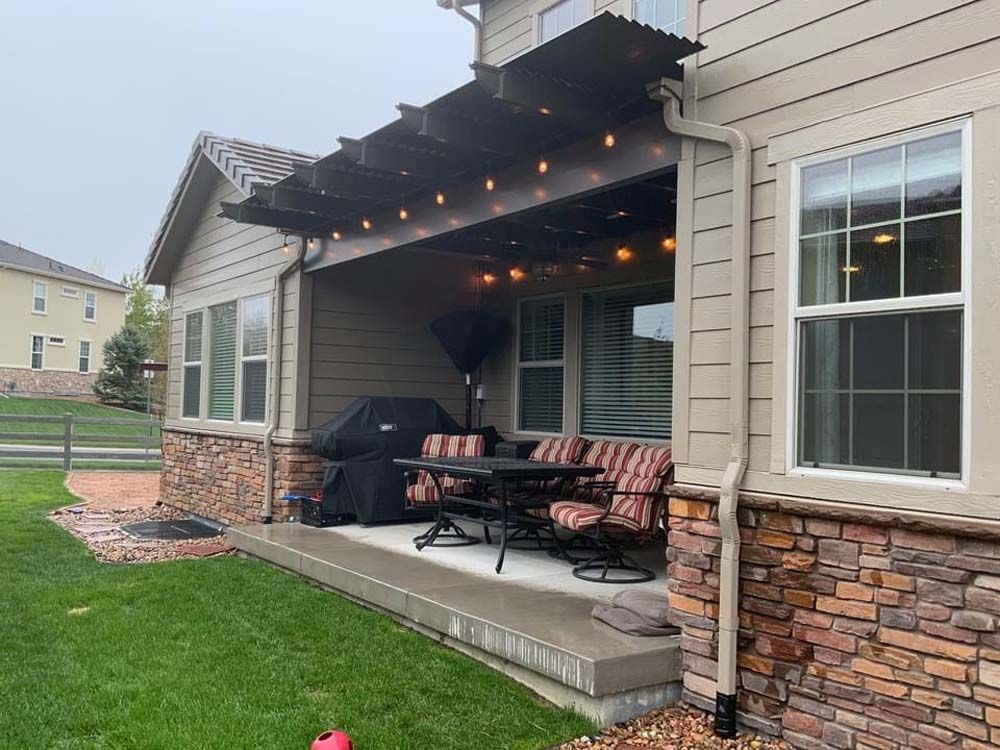 Backyard patio with string lights, dining set, and grill under a pergola roof.