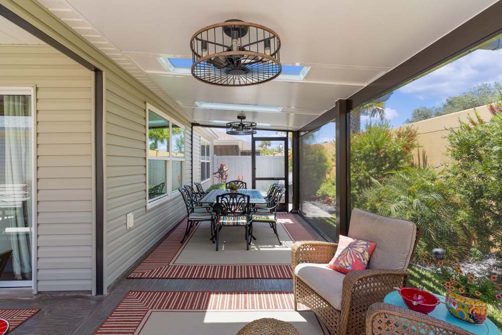 Screened patio with dining table, seating, fans, and garden view.