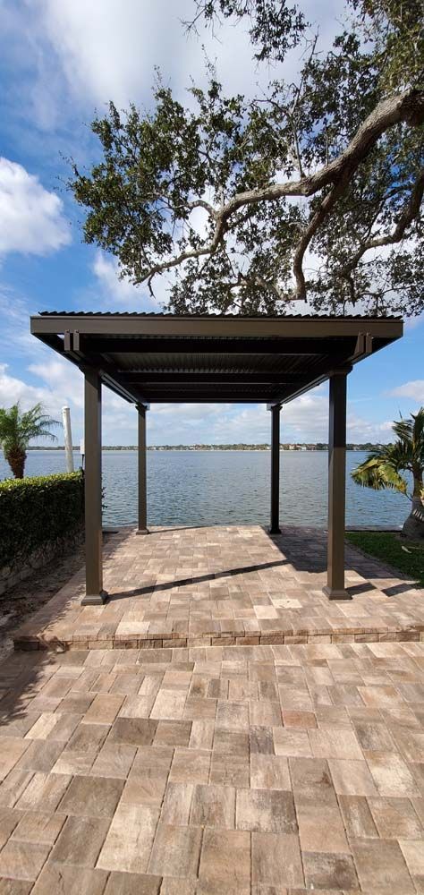 A covered structure overlooking a body of water, on a brick patio, under a blue sky.