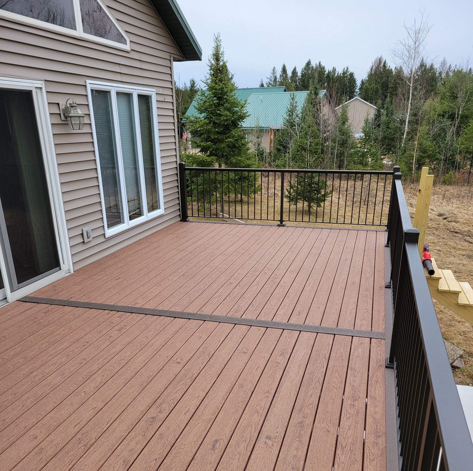 A large wooden deck with a metal railing and a house in the background