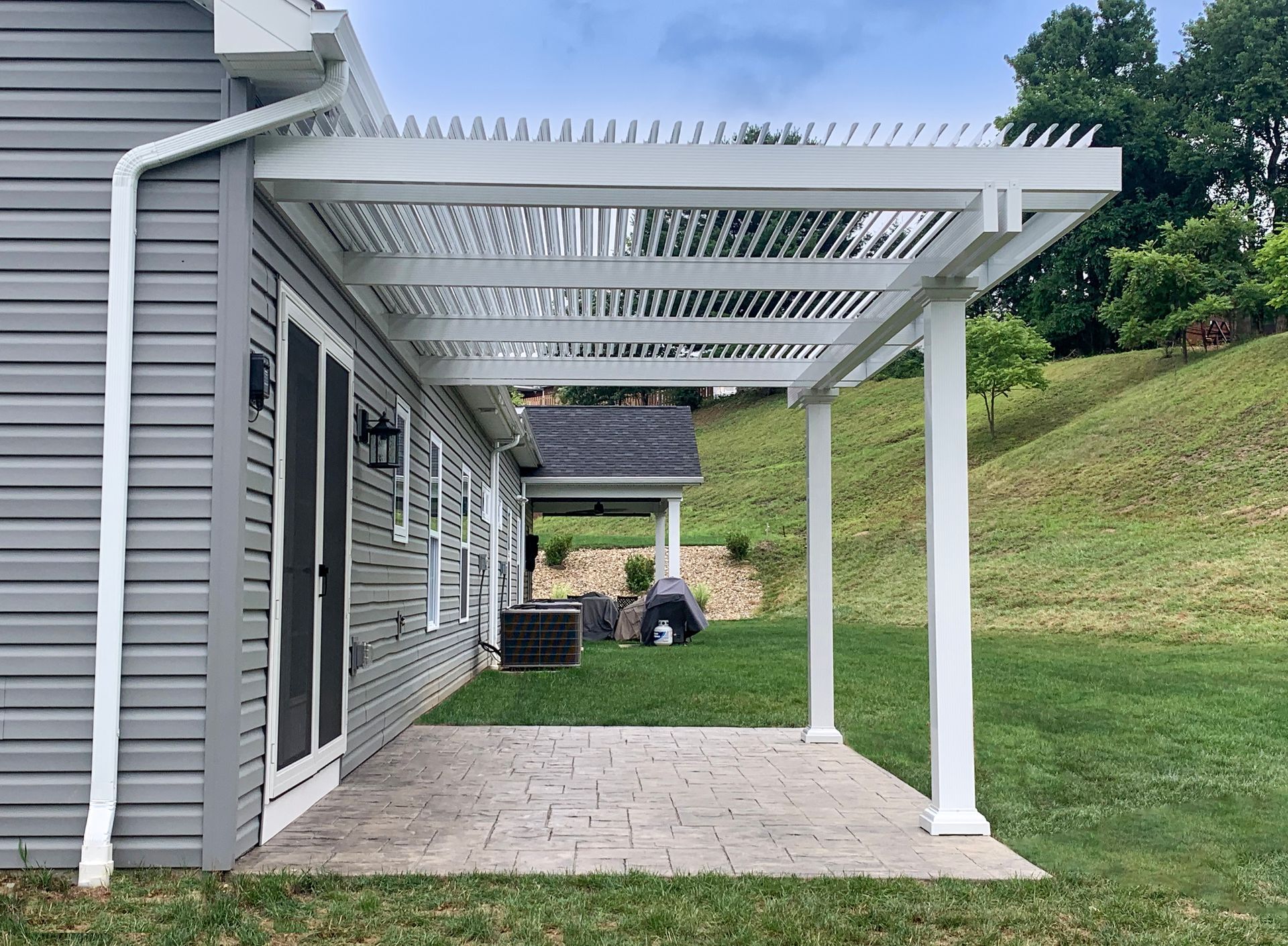 A modern wooden deck with a slatted pergola, featuring an outdoor dining set and bar stools overlooking a green yard.