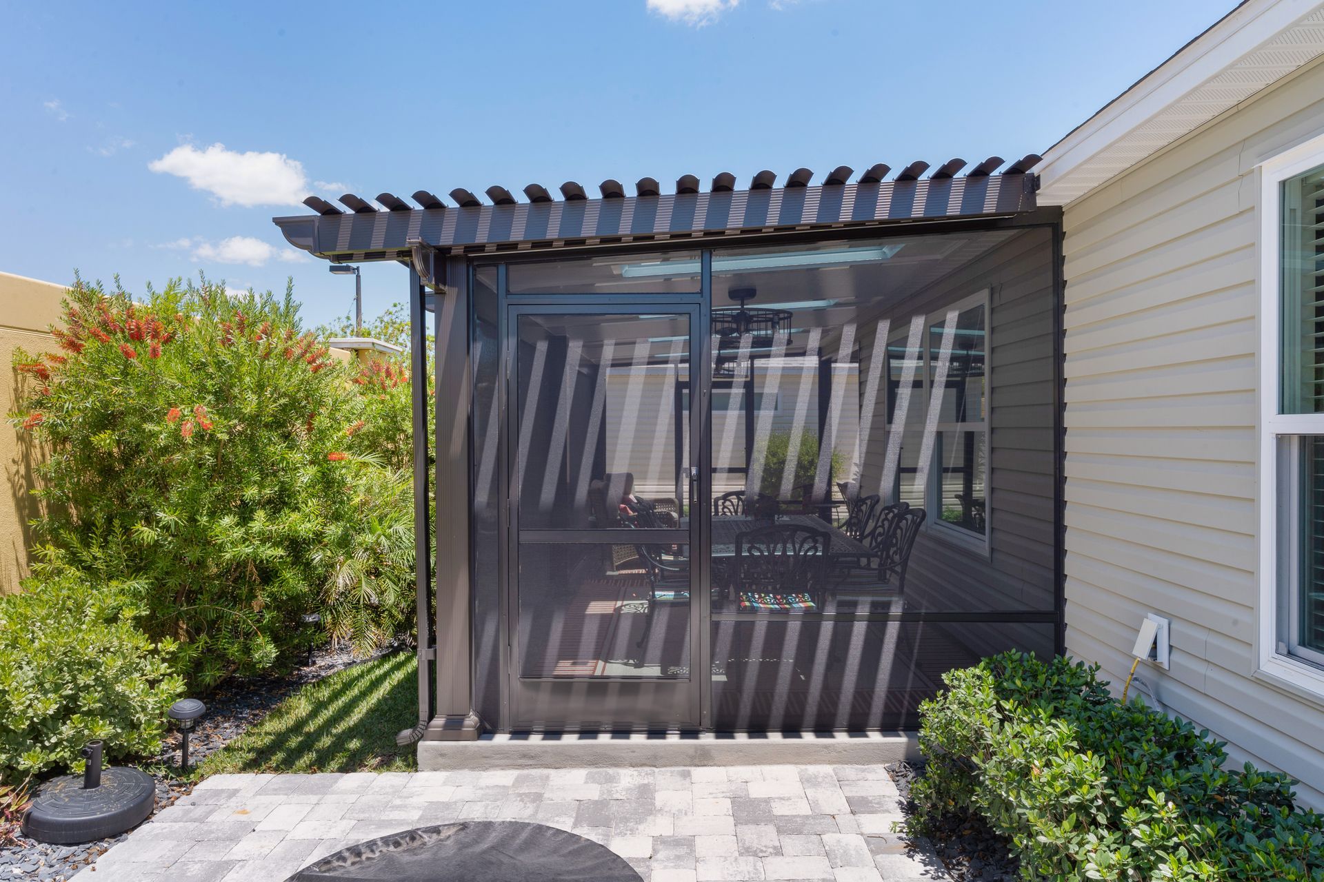 A backyard pergola with a retractable privacy screen attached to the side of a house next to a manicured lawn.