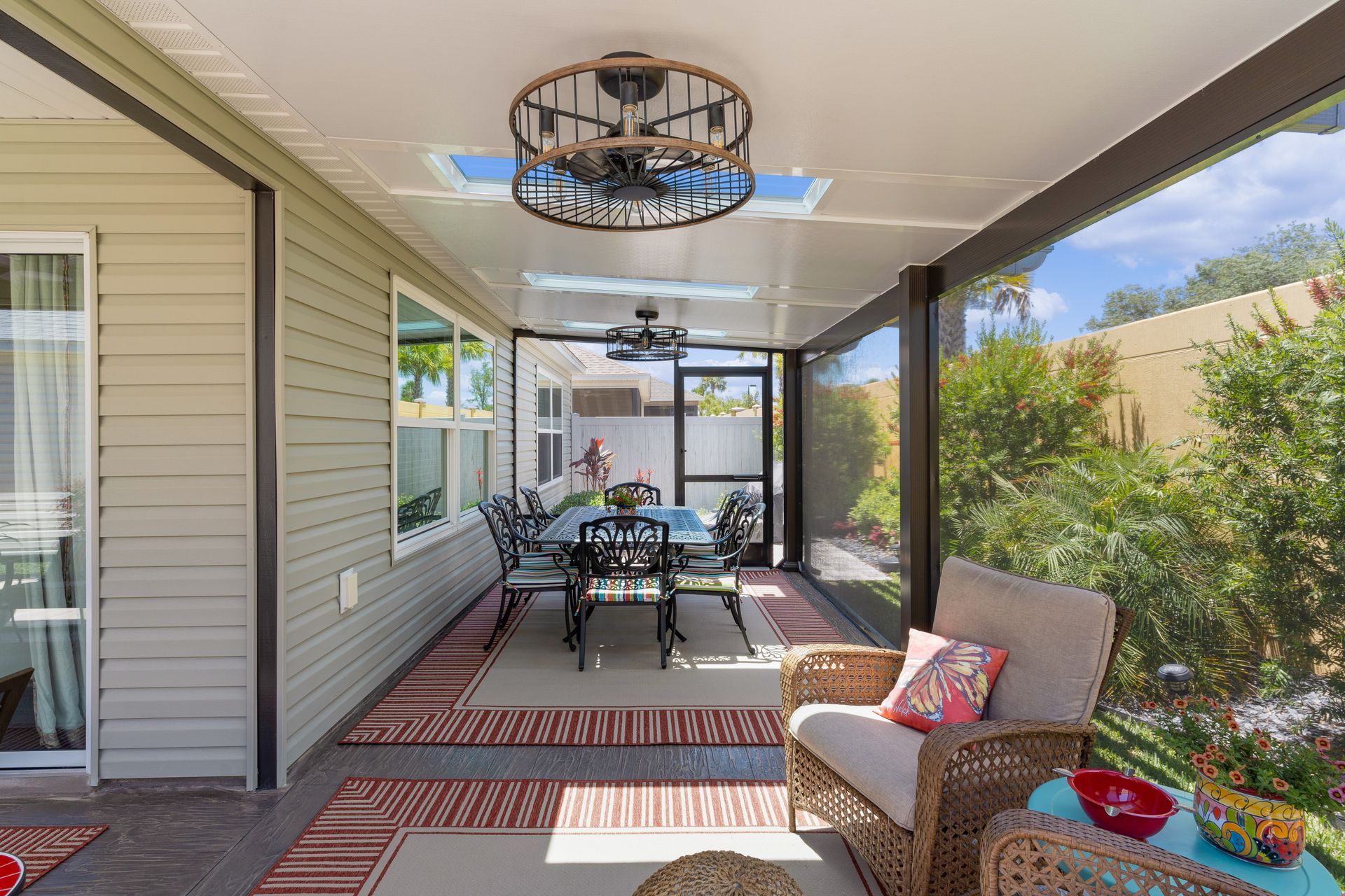 A covered, screened-in patio features a dining set, a wicker armchair, and a decorative ceiling light with a fan.