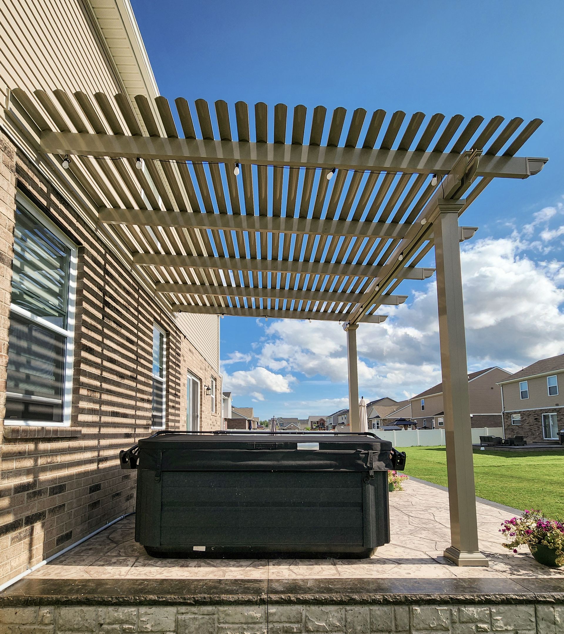 A brown corrugated metal patio roof extends from a support beam and post against a cloudy blue sky.