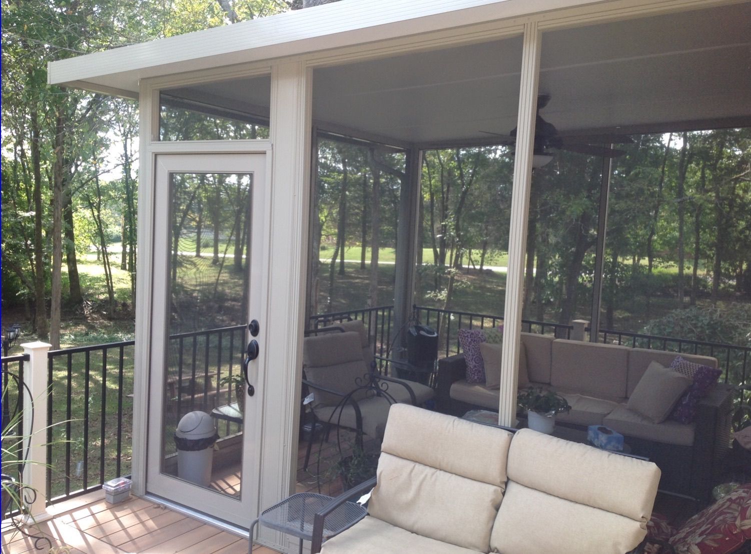 A screened-in deck featuring a glass door, outdoor furniture, and a view of trees in the background.