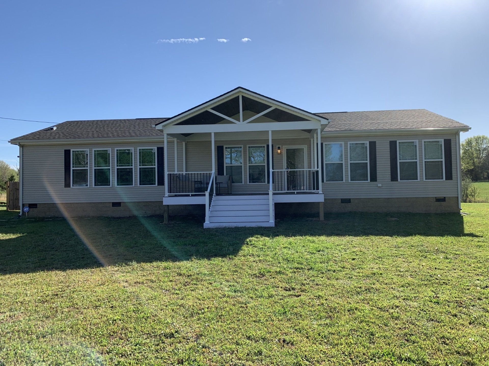 A house with a porch and stairs is sitting on top of a lush green field.