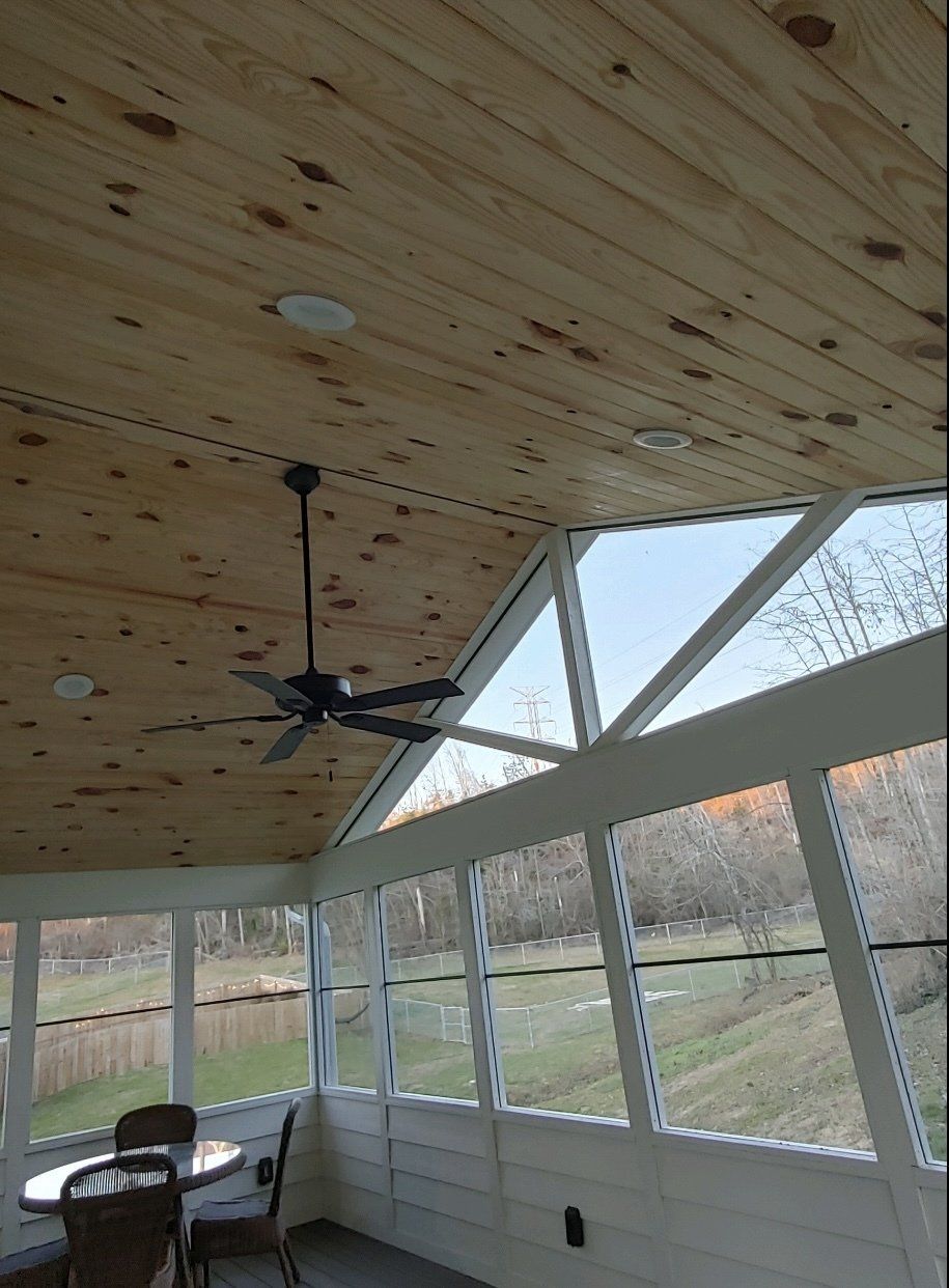 A screened in porch with a table and chairs and a ceiling fan