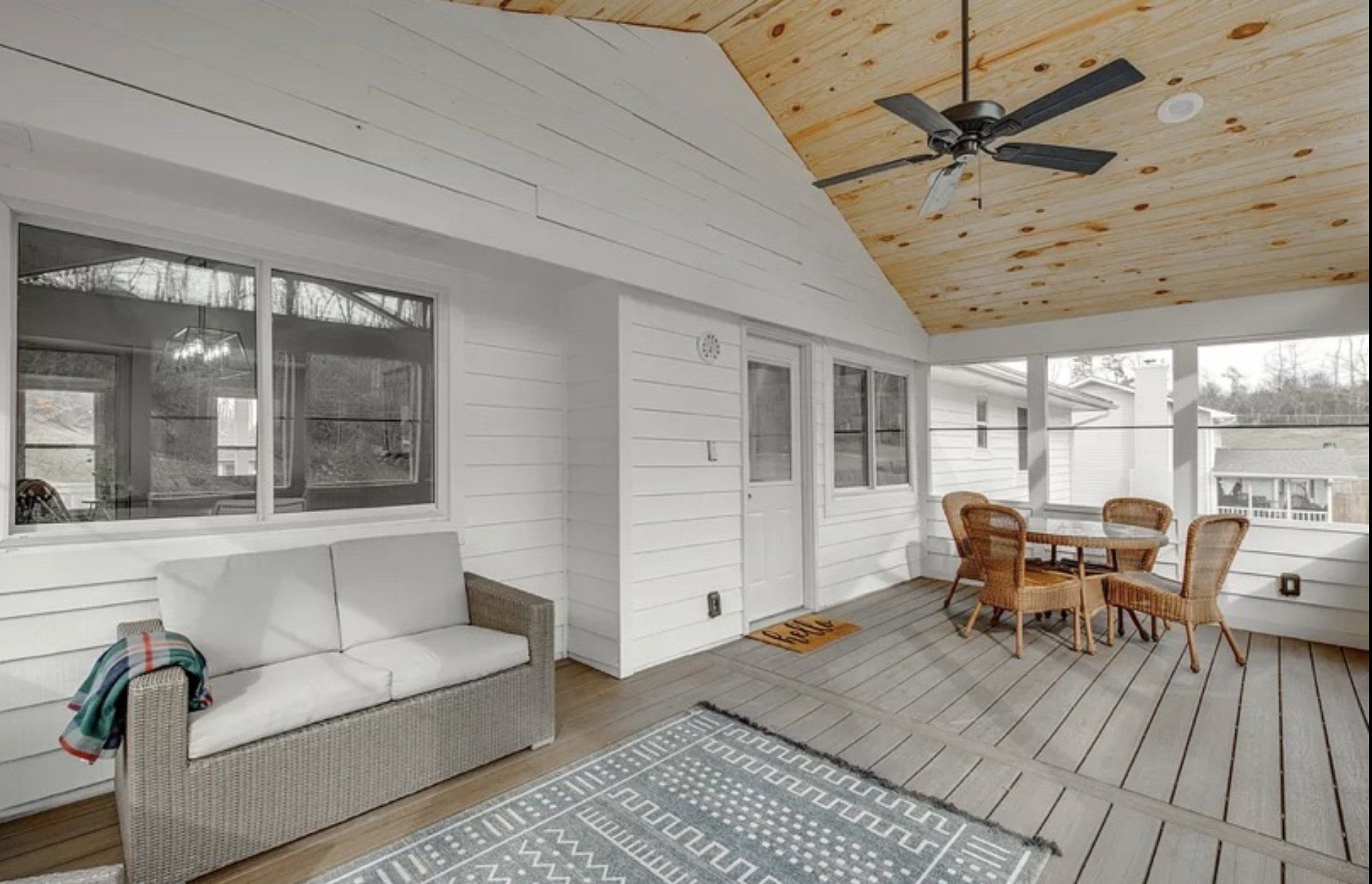 A screened in porch with a couch , table and chairs and a ceiling fan.