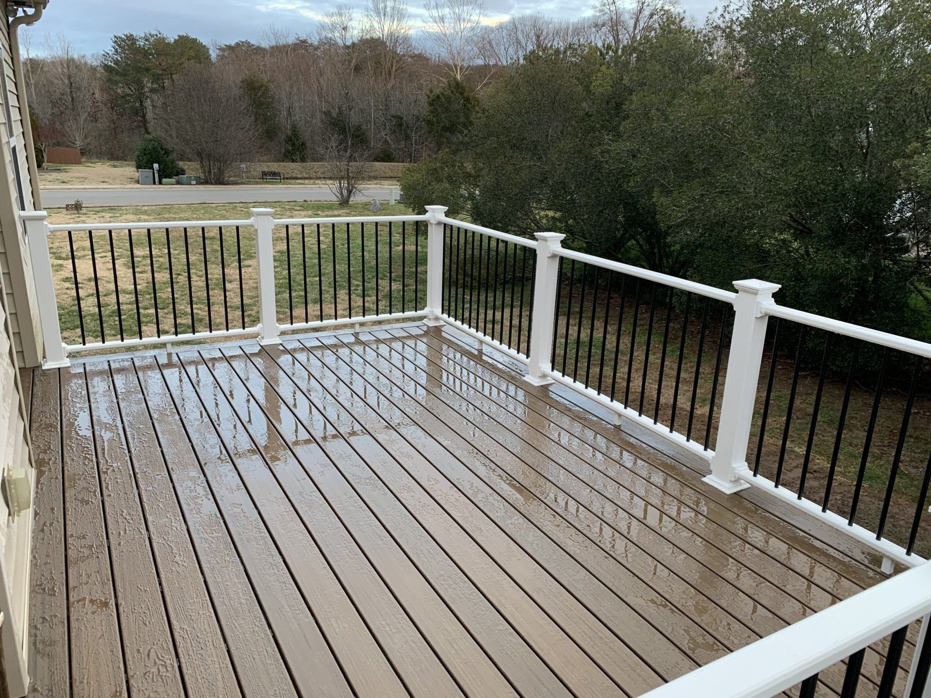 A large wooden deck with a white railing and trees in the background.