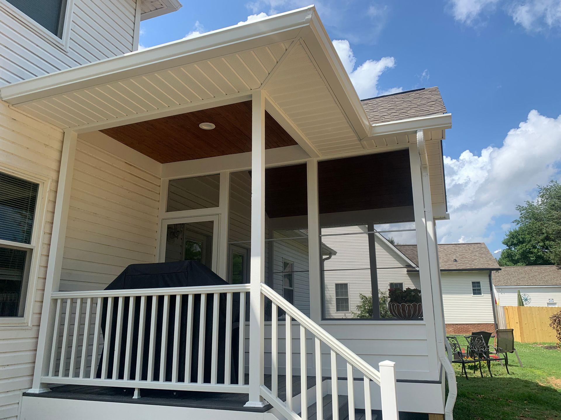 A white house with a screened in porch and a grill on it.