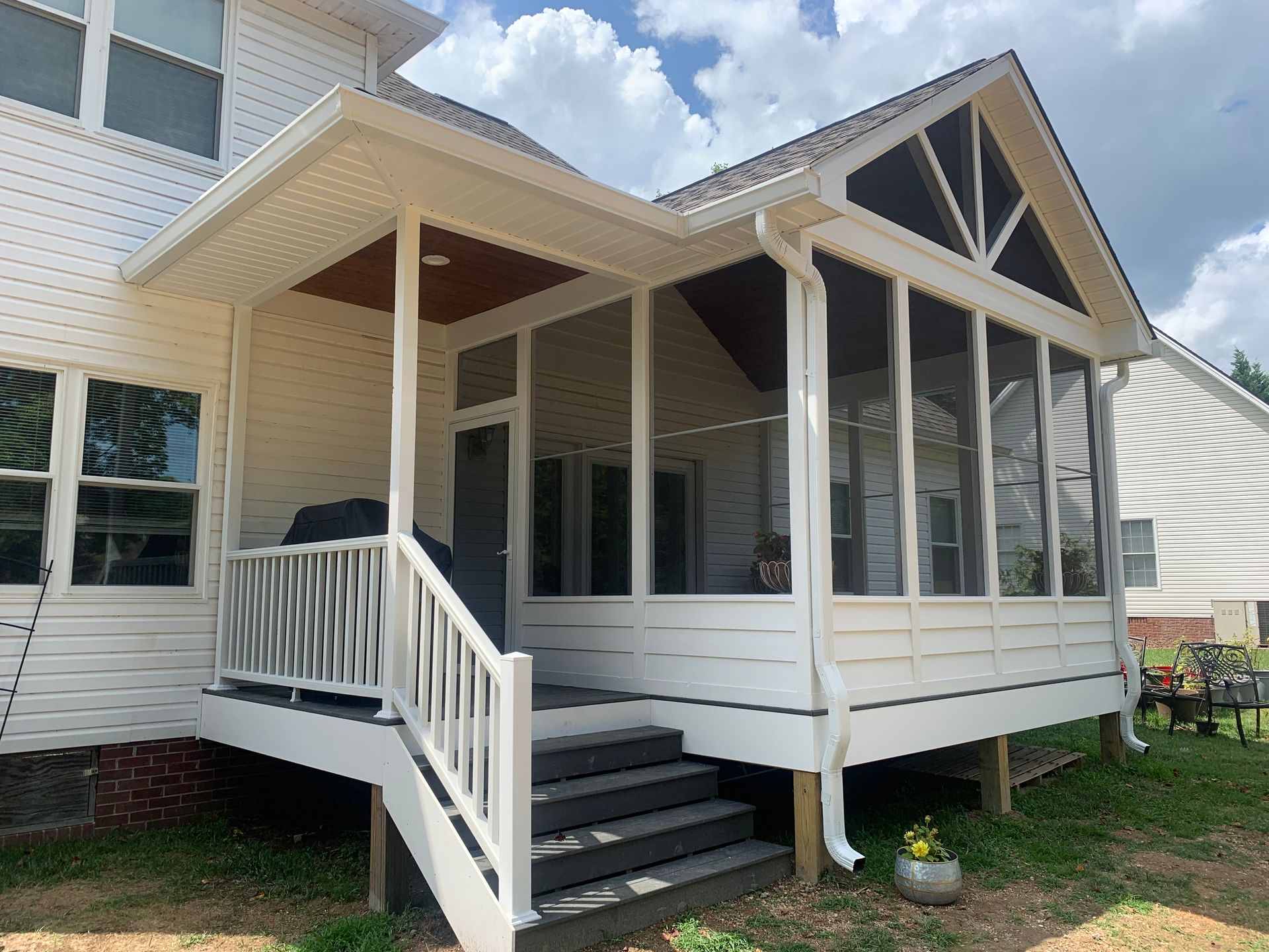 A screened in porch with stairs leading up to it is in the backyard of a house.