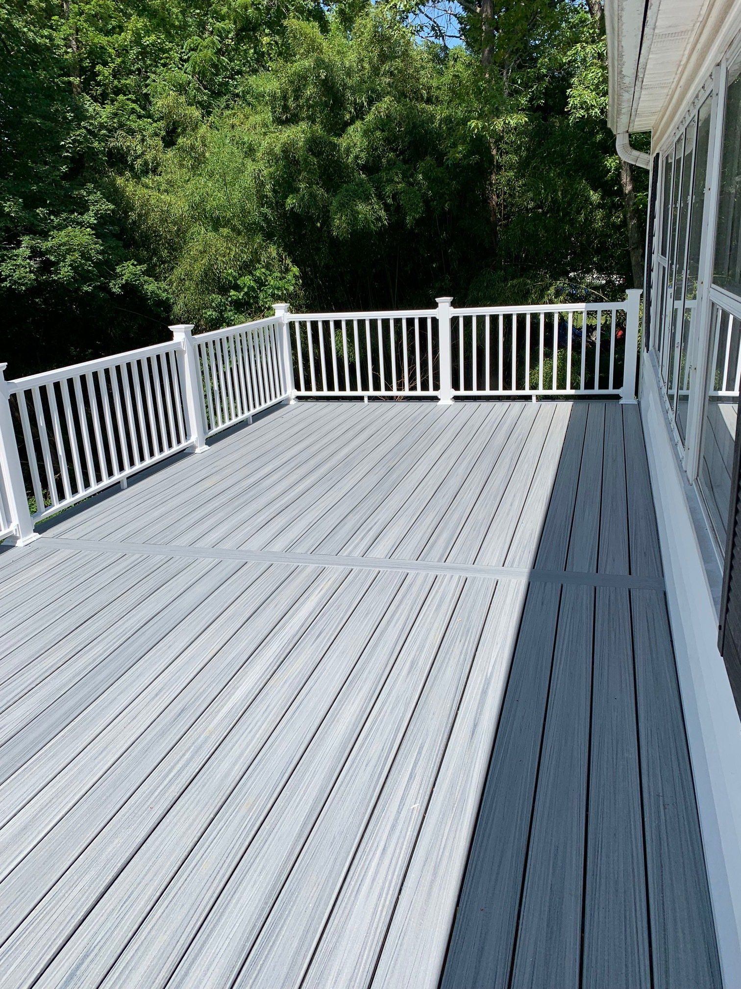 A large gray deck with a white railing and trees in the background.