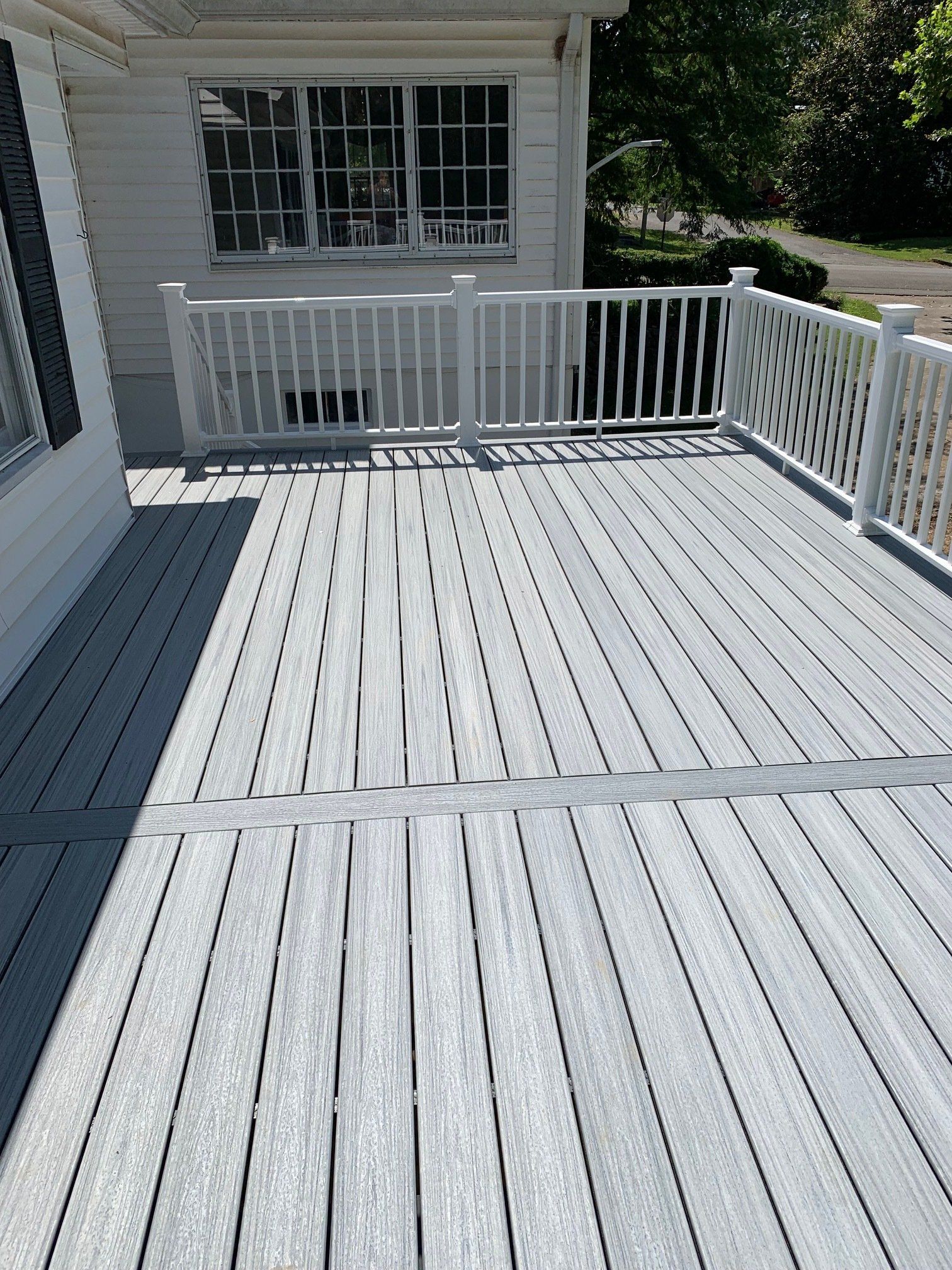 A white deck with a white railing is sitting in front of a white house.