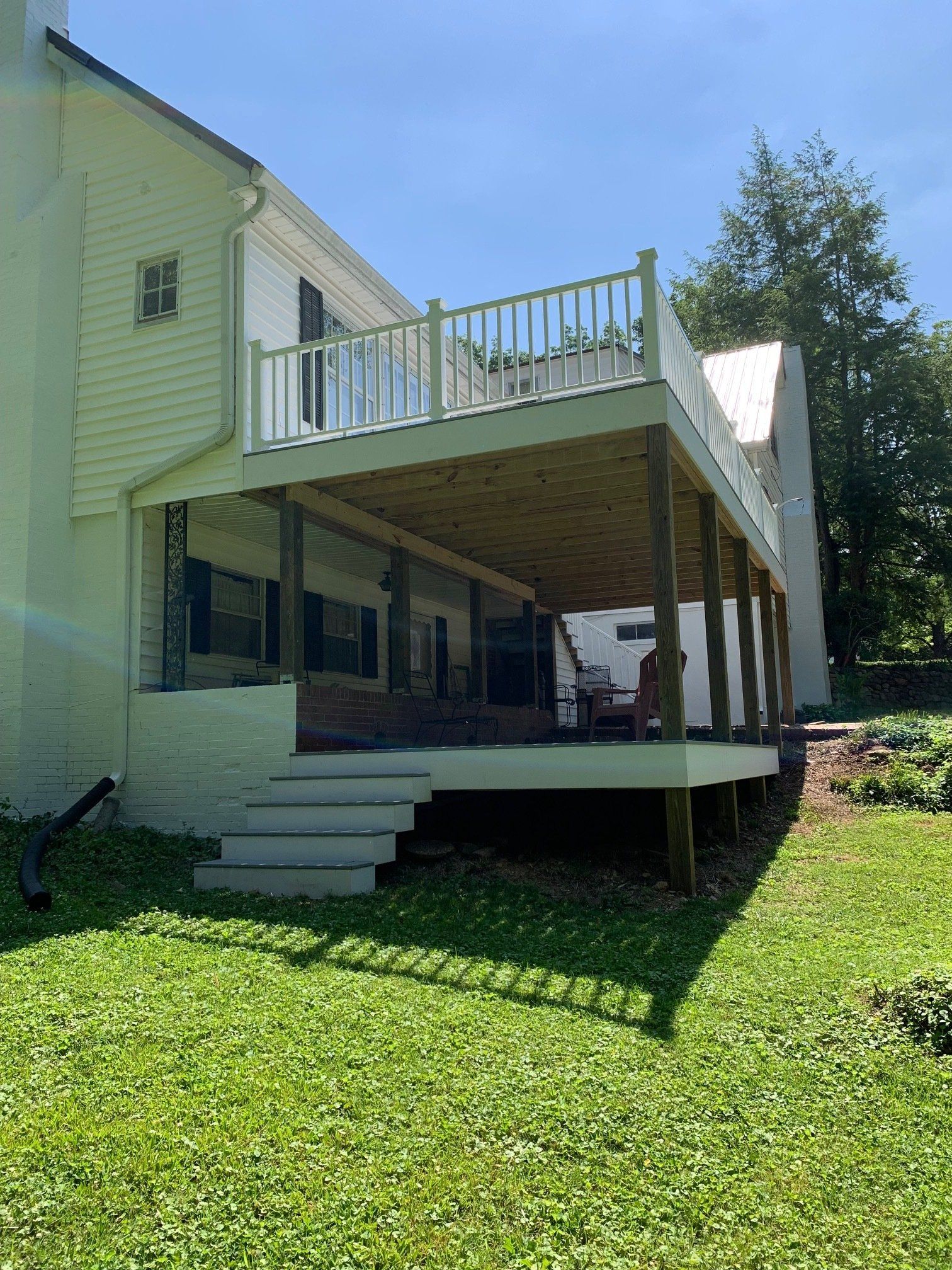 A large deck with stairs leading up to it is in the backyard of a house.