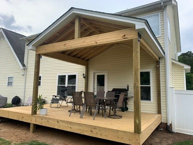A wooden deck with a table and chairs on it in front of a house.