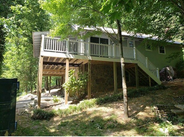A house with a large deck on the side of it surrounded by trees.