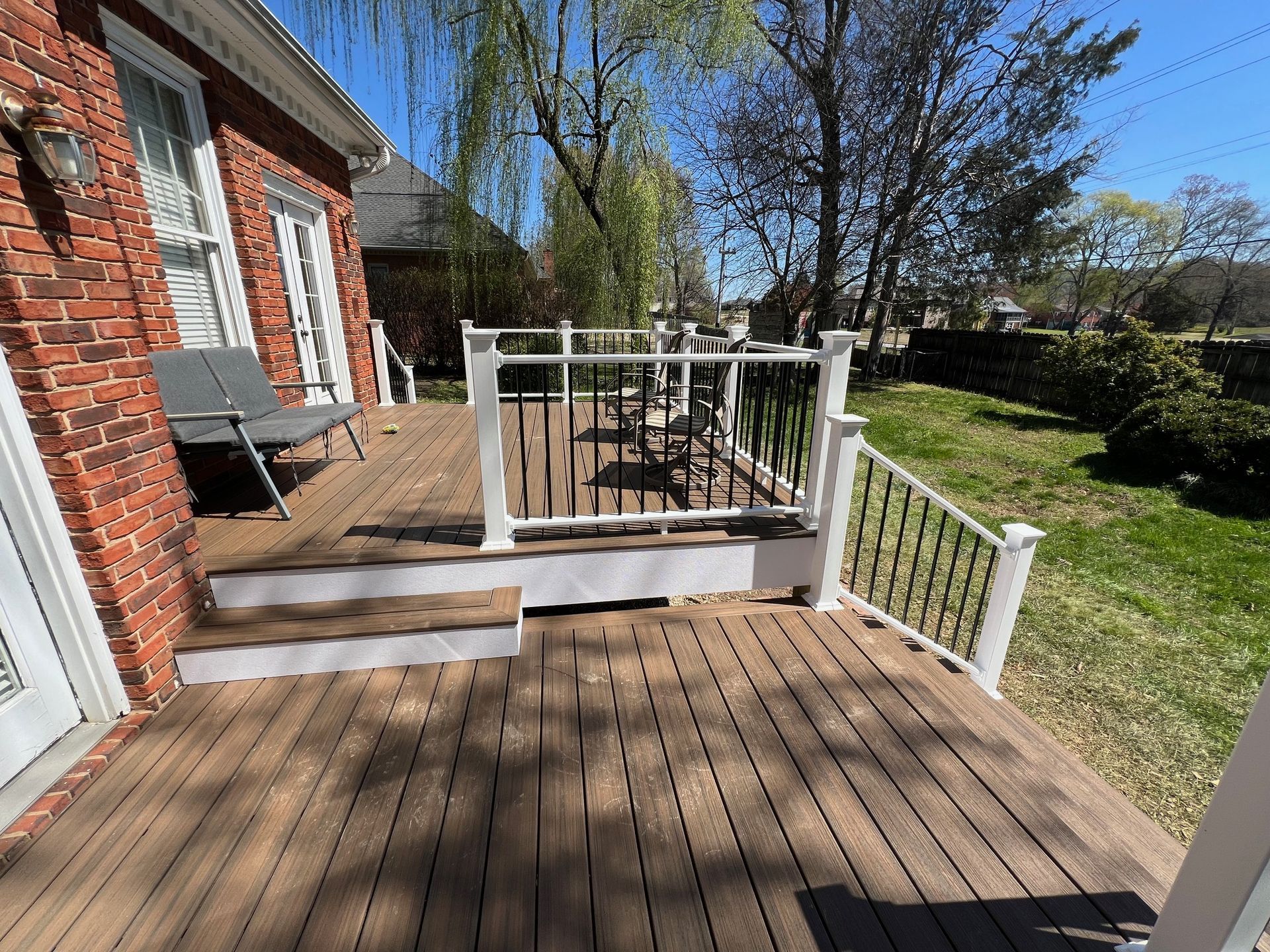 A wooden deck with a white railing and stairs in front of a brick house.