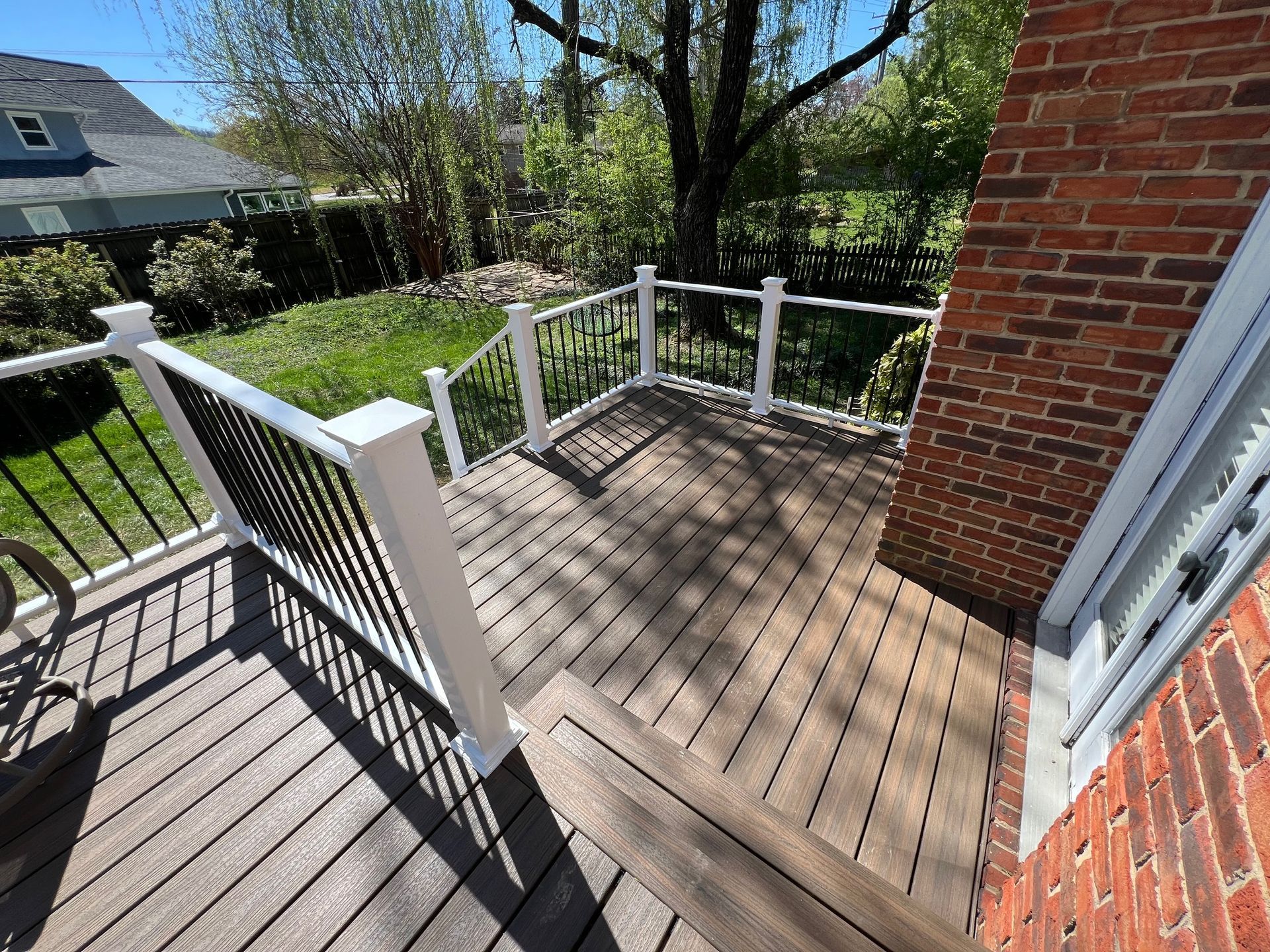 A wooden deck with a white railing and a brick building in the background.