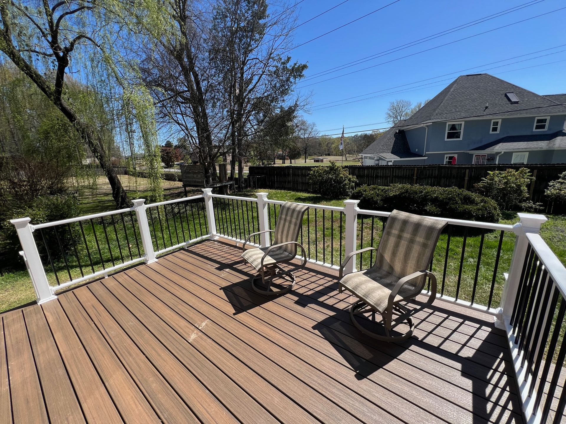 There are two rocking chairs on the deck of a house.