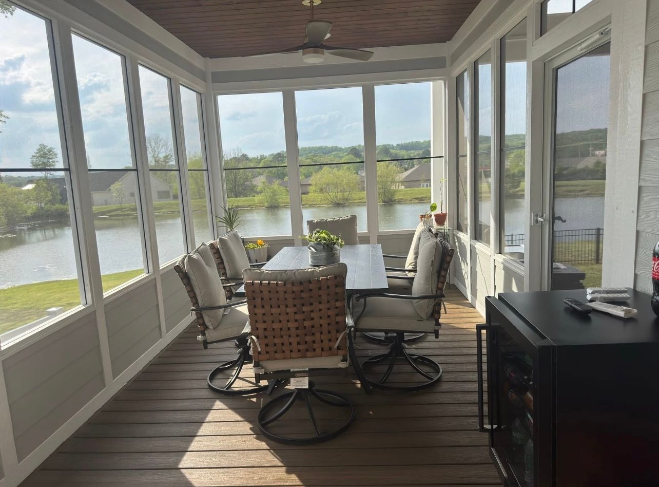 A screened in porch with a table and chairs and a view of a lake.