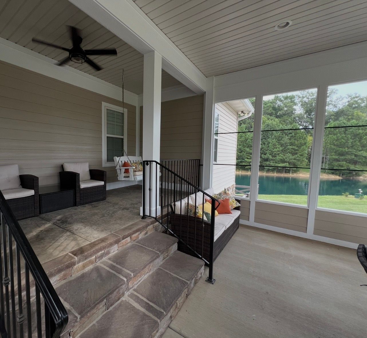 Covered porch with seating, steps, and windows overlooking a lake.