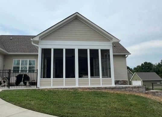Screened-in porch on a beige house with white trim. Green grass and overcast sky.