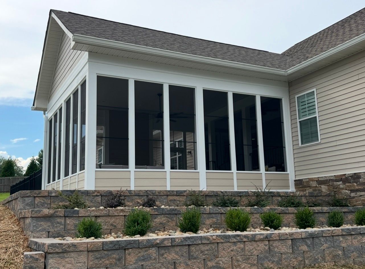 Screened-in porch addition with white trim, beige siding, and a stone retaining wall.