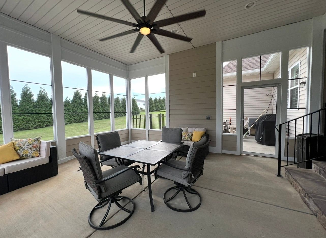 Screened-in patio with outdoor furniture, ceiling fan, and view of a yard with trees.