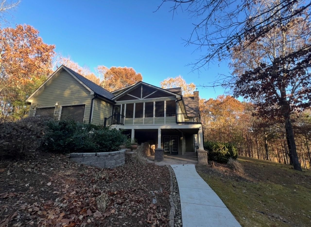 House with green siding and screen porch, surrounded by fall foliage, concrete walkway.