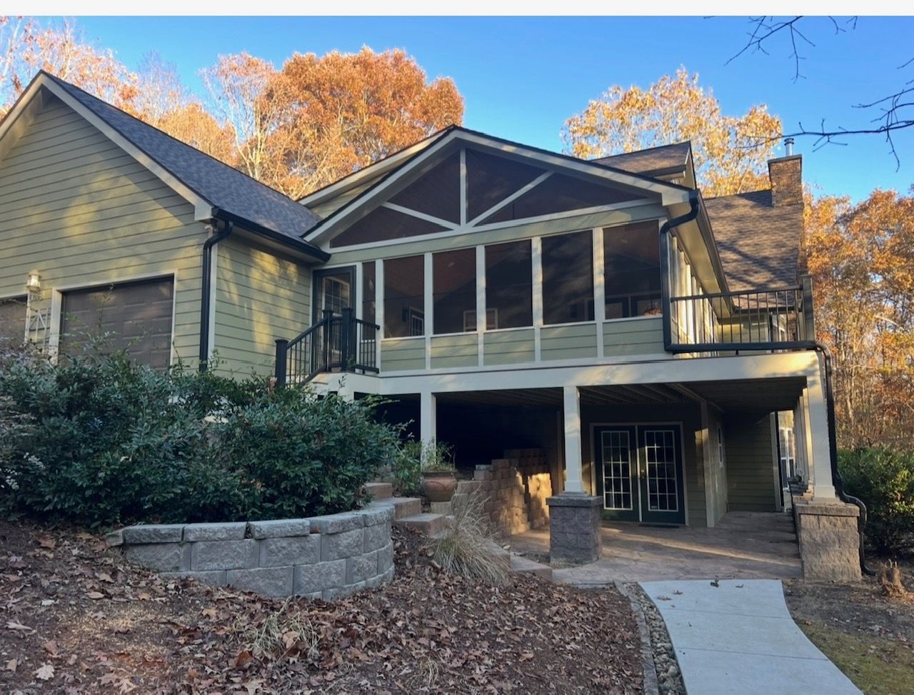 Green house with screened porch, chimney, and walkway. Autumn foliage in background.