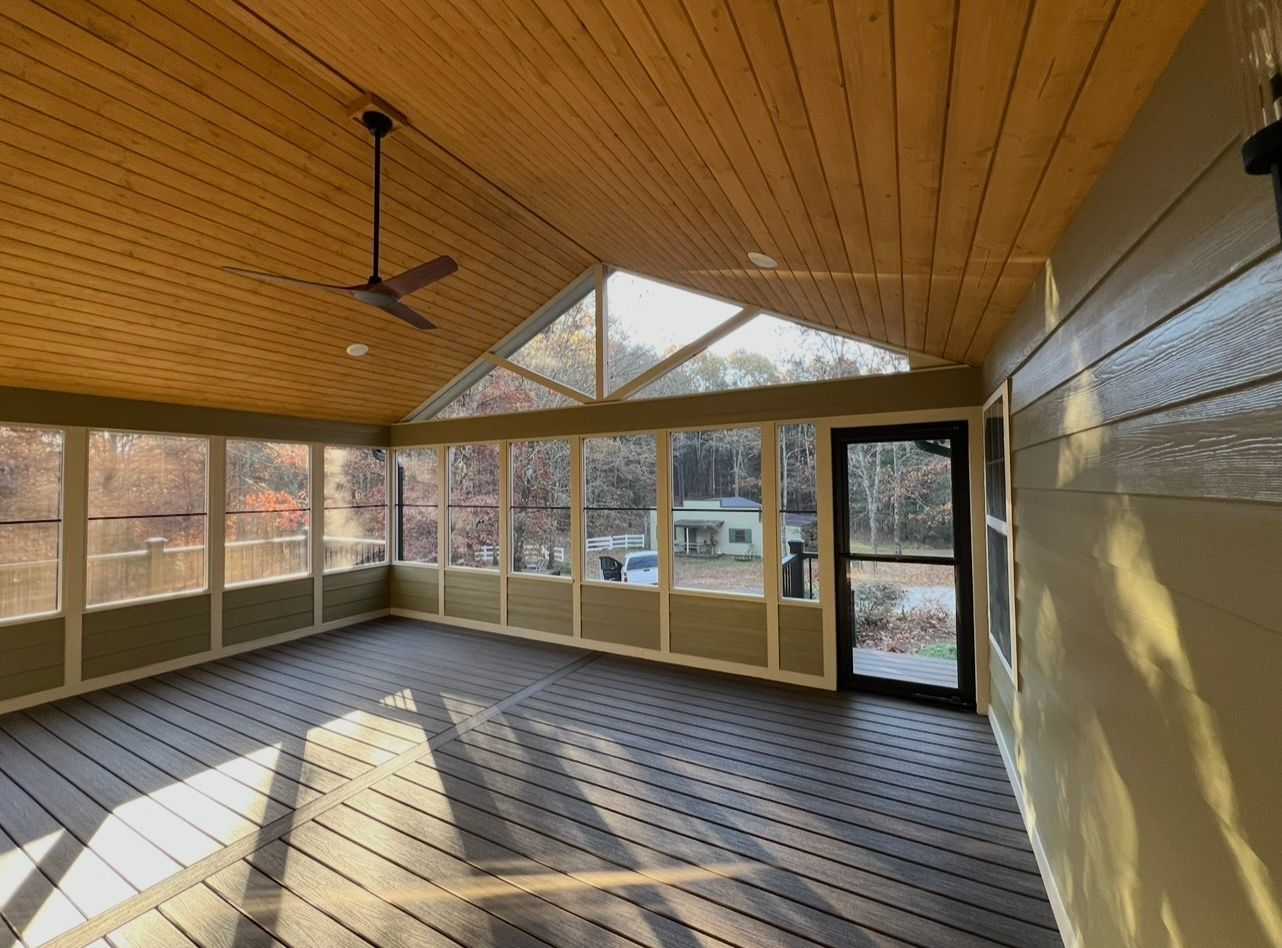 Screened porch with wooden ceiling, gray flooring, glass windows, and a black door.