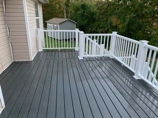 A gray deck with a white railing and a shed in the background.