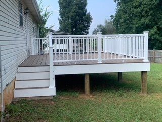 A large deck with a white railing is in the backyard of a house.
