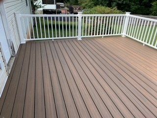 A brown deck with a white railing and a white fence.