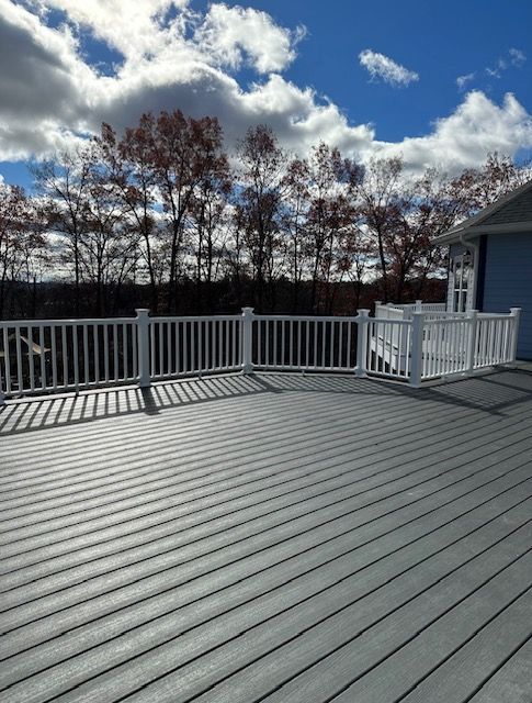 A gray deck with a white railing and trees in the background