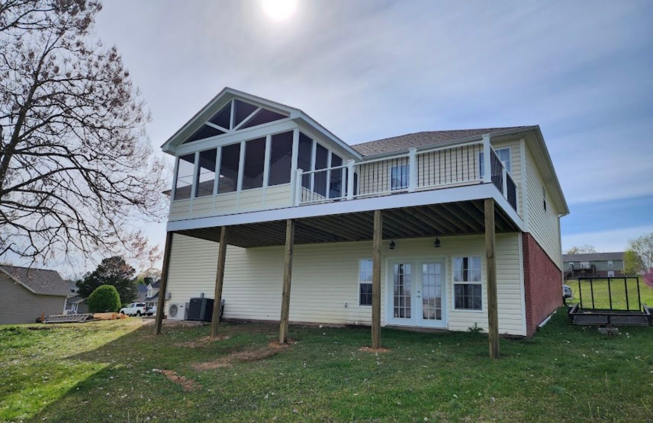 The back of a house with a screened in porch and a large deck.