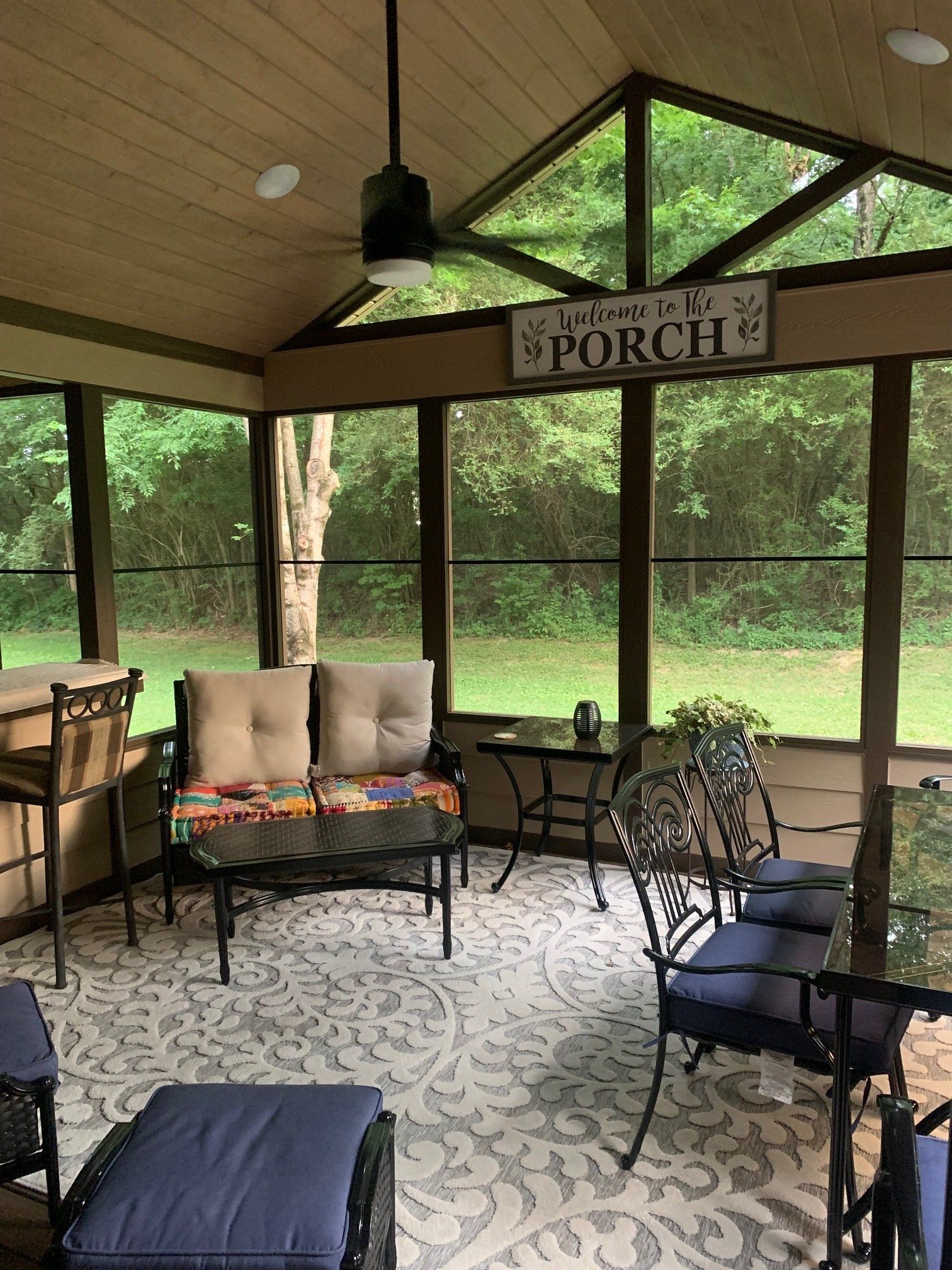 A screened in porch with furniture and a sign that says `` welcome to the porch ''.