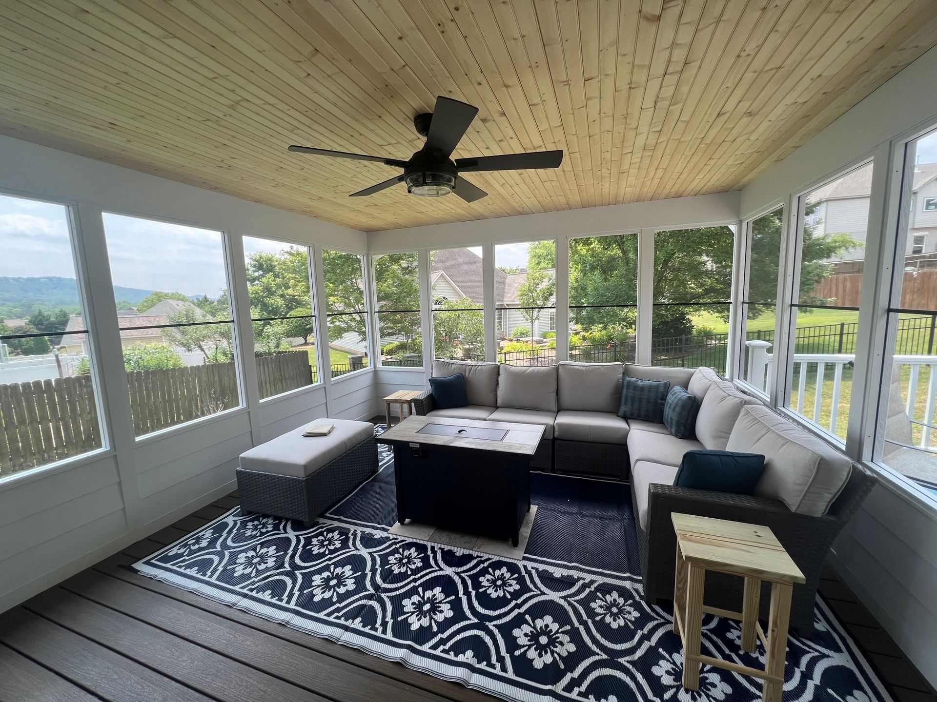 A screened in porch with a sectional couch and a ceiling fan.