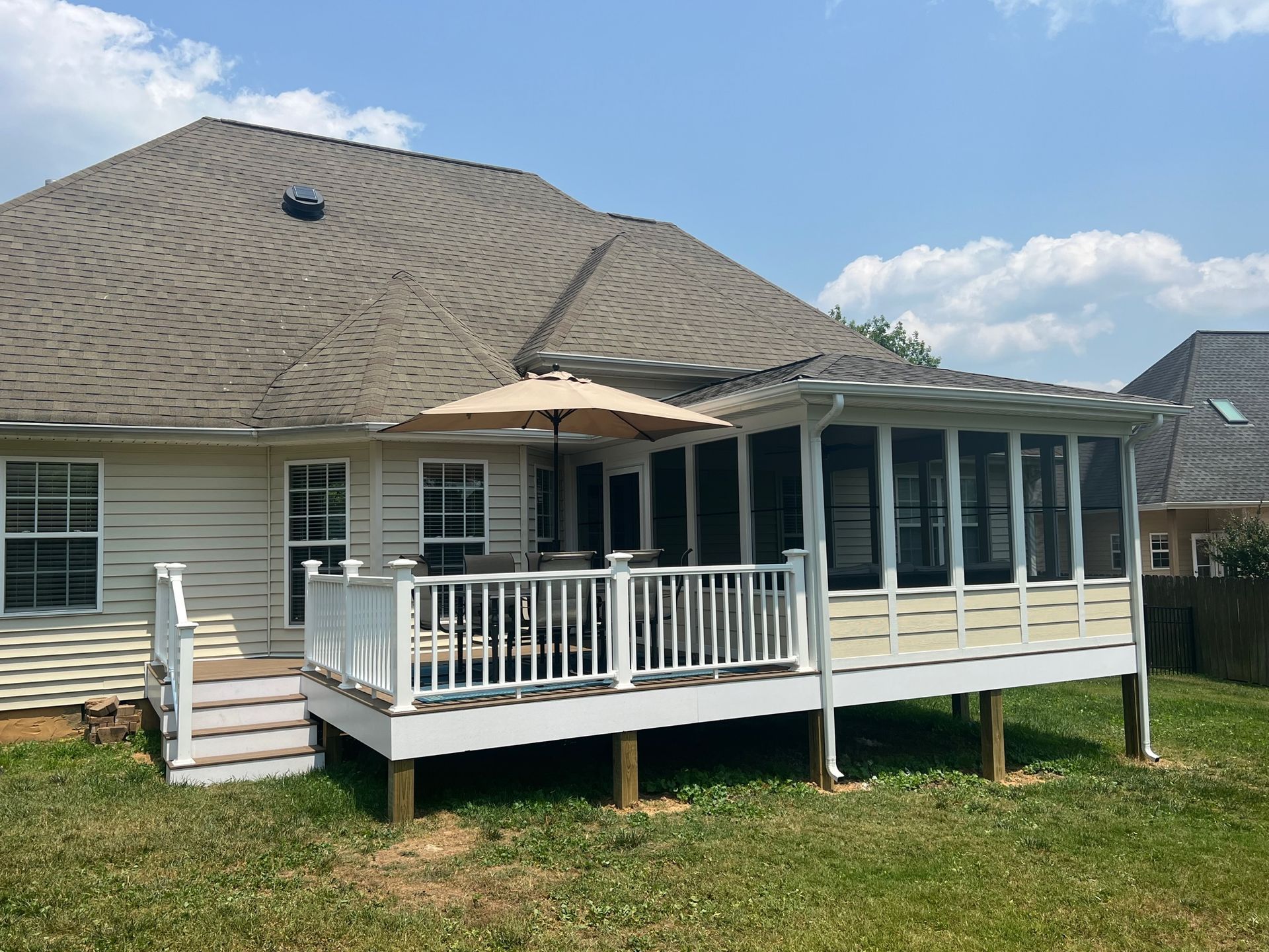 The back of a house with a screened in porch and umbrella.